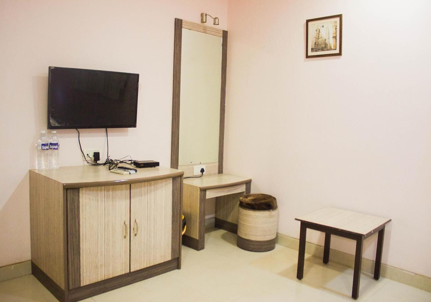 A small room with a wooden cabinet, a television, a mirror, a small table, and a trash bin.