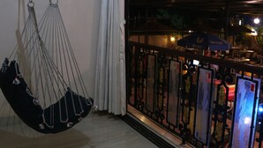 Una habitación con una silla colgante, un balcón con barandilla de metal y vista a la calle.
