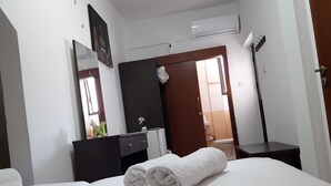 A hotel room with a bed, a dresser, a mirror, a door, and an air conditioning unit. - Marina's Rooms (Larnaca)