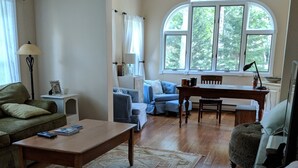 Un salon comprenant un canapé, une table basse, une table à manger et une fenêtre donnant sur des arbres.