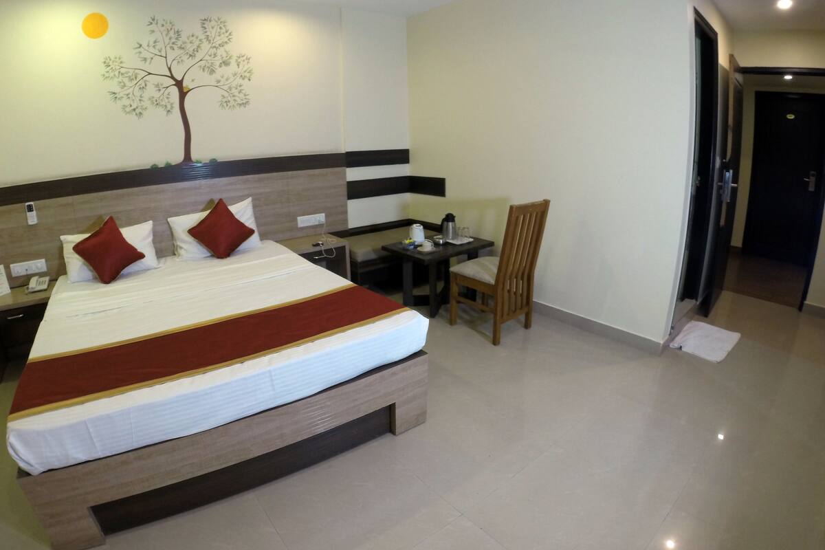 A hotel room with a large bed, a desk, a chair, and a wall-mounted tree decoration.