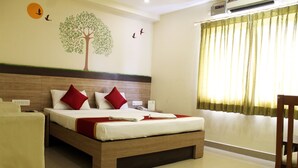 Une chambre d’hôtel avec un lit en bois, des oreillers rouges et blancs, une fresque représentant un arbre sur un mur, et une fenêtre avec des rideaux.