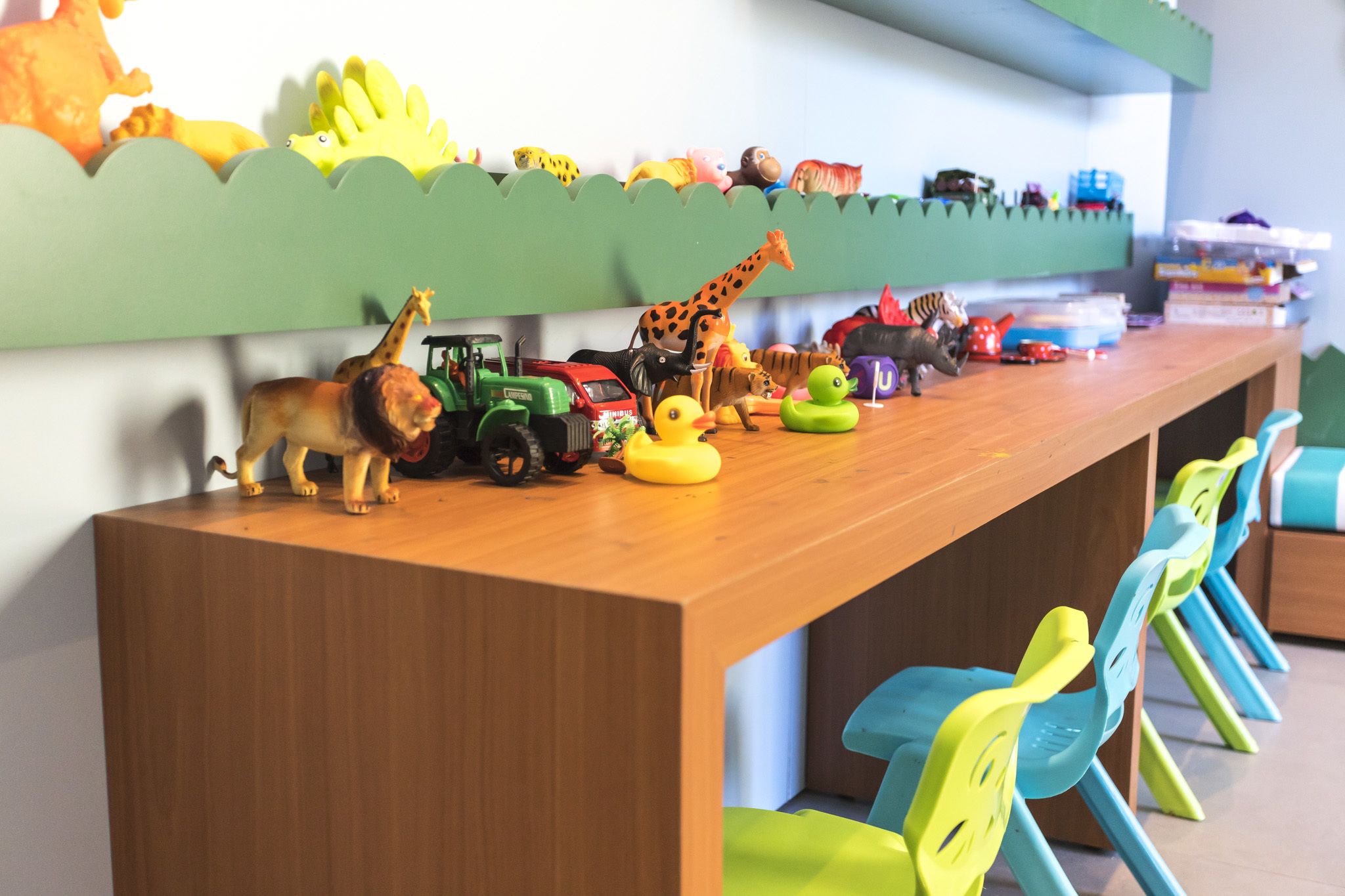 Un área de juegos infantiles con una larga mesa de madera que exhibe diversos vehículos y animales de juguete.