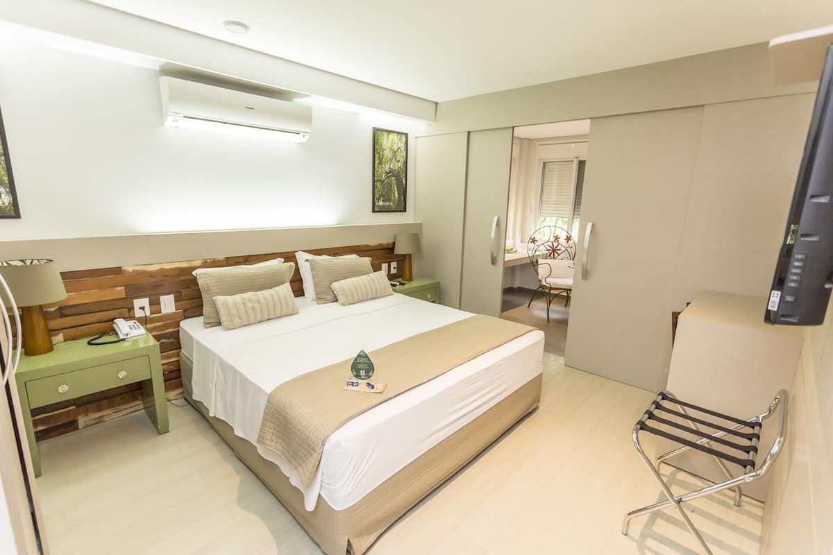 A hotel room with a large bed, a bedside table with a lamp, a chair, and a television.