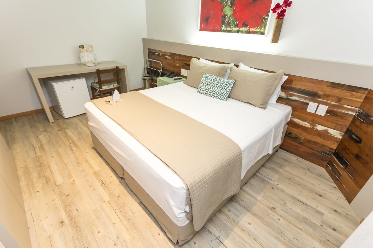 A bedroom with a bed, a desk, a small refrigerator, and a wooden headboard.