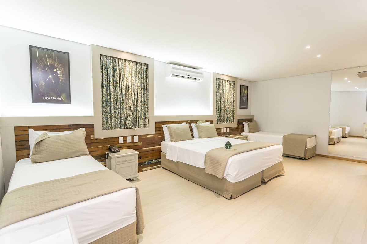 A hotel room with two beds, a small bedside table, a mirror, and a large window with curtains.