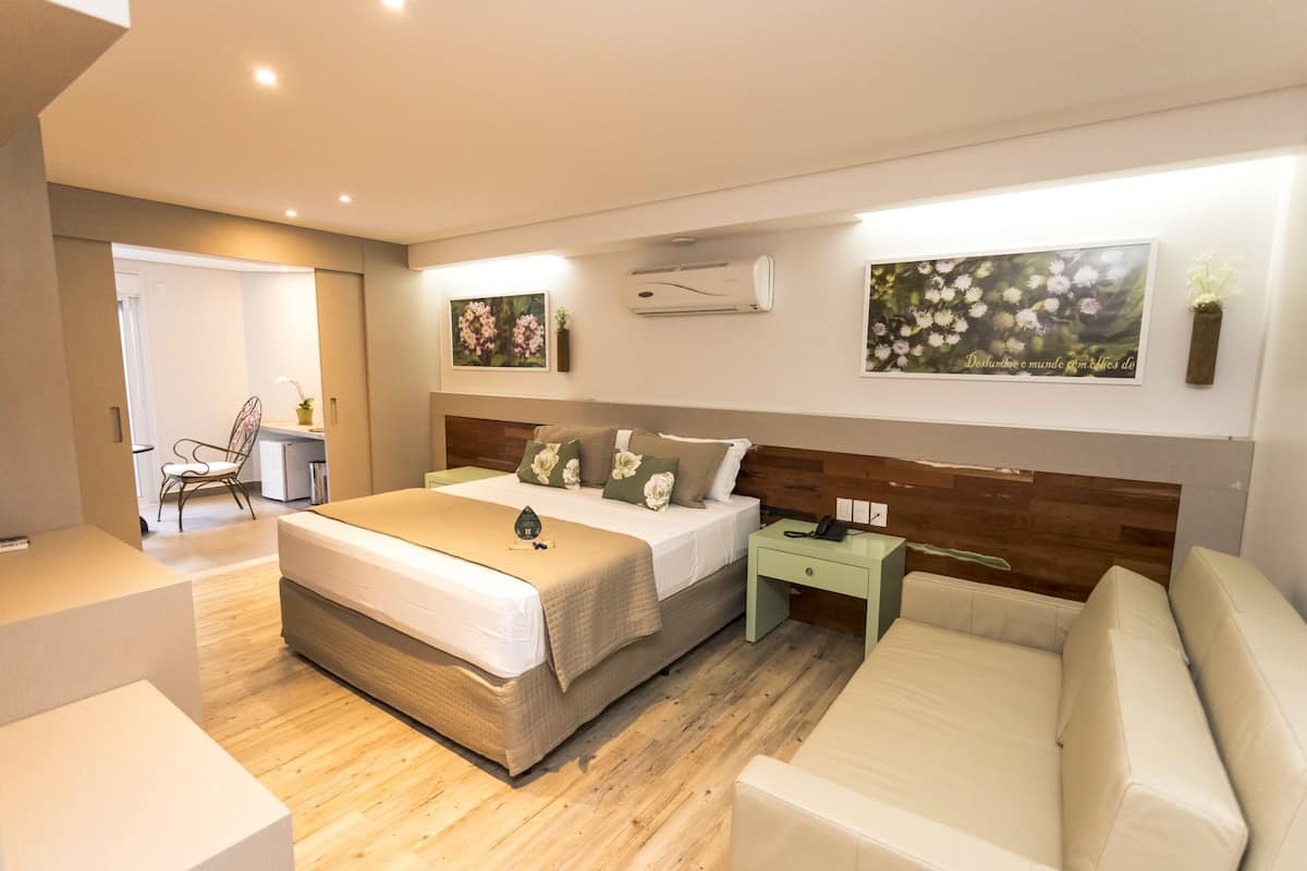 A modern hotel room with a large bed, a bedside table, a chair, and a sofa.