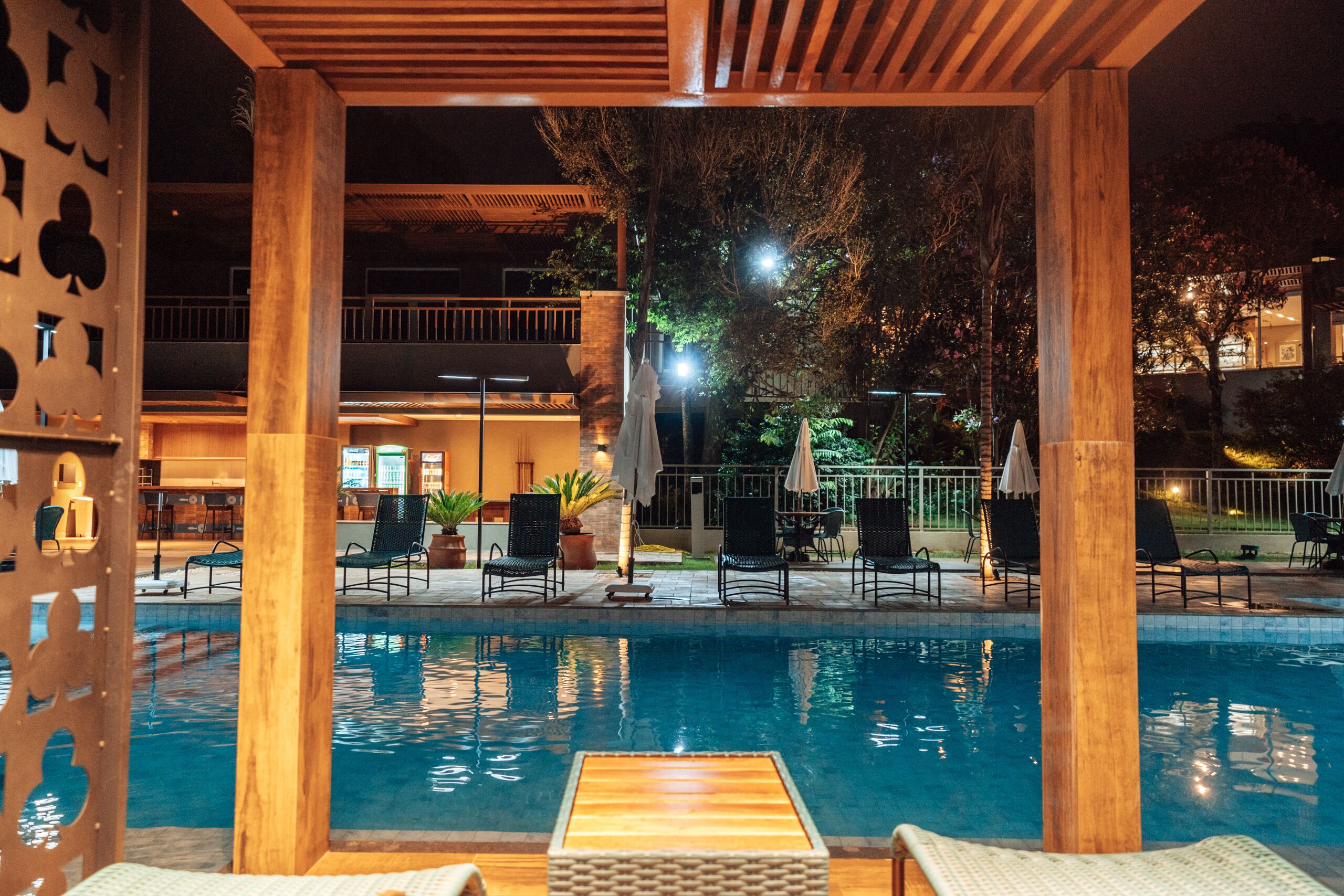 Un espace piscine agrémenté de piliers en bois, de chaises longues et offrant une vue sur le bâtiment en arrière-plan.