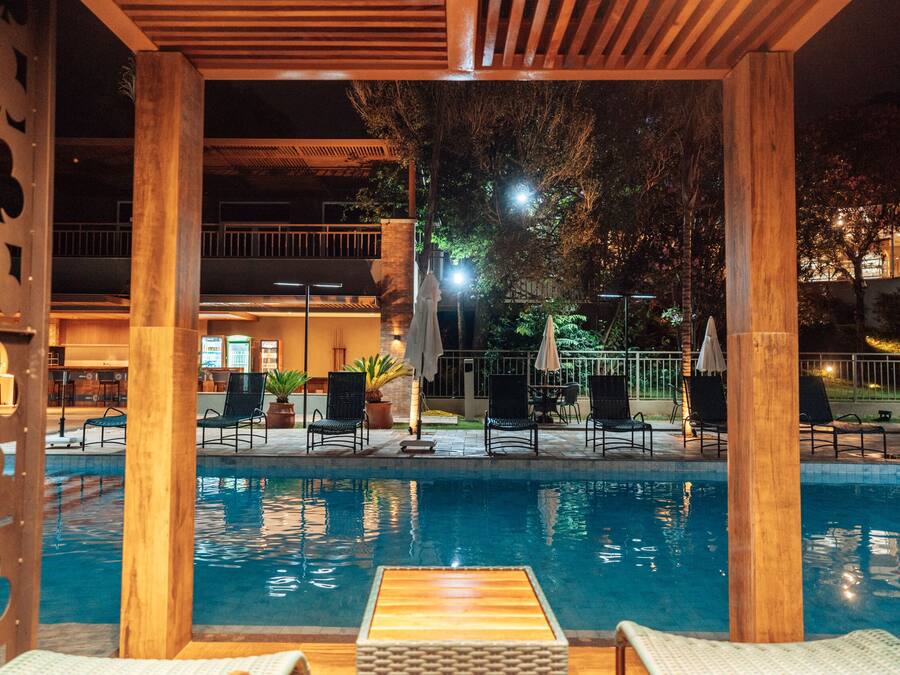 Un espace piscine agrémenté de piliers en bois, de chaises longues et offrant une vue sur le bâtiment en arrière-plan.