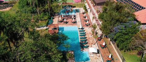 An aerial view of a resort with a swimming pool, sun loungers, and a tennis court.