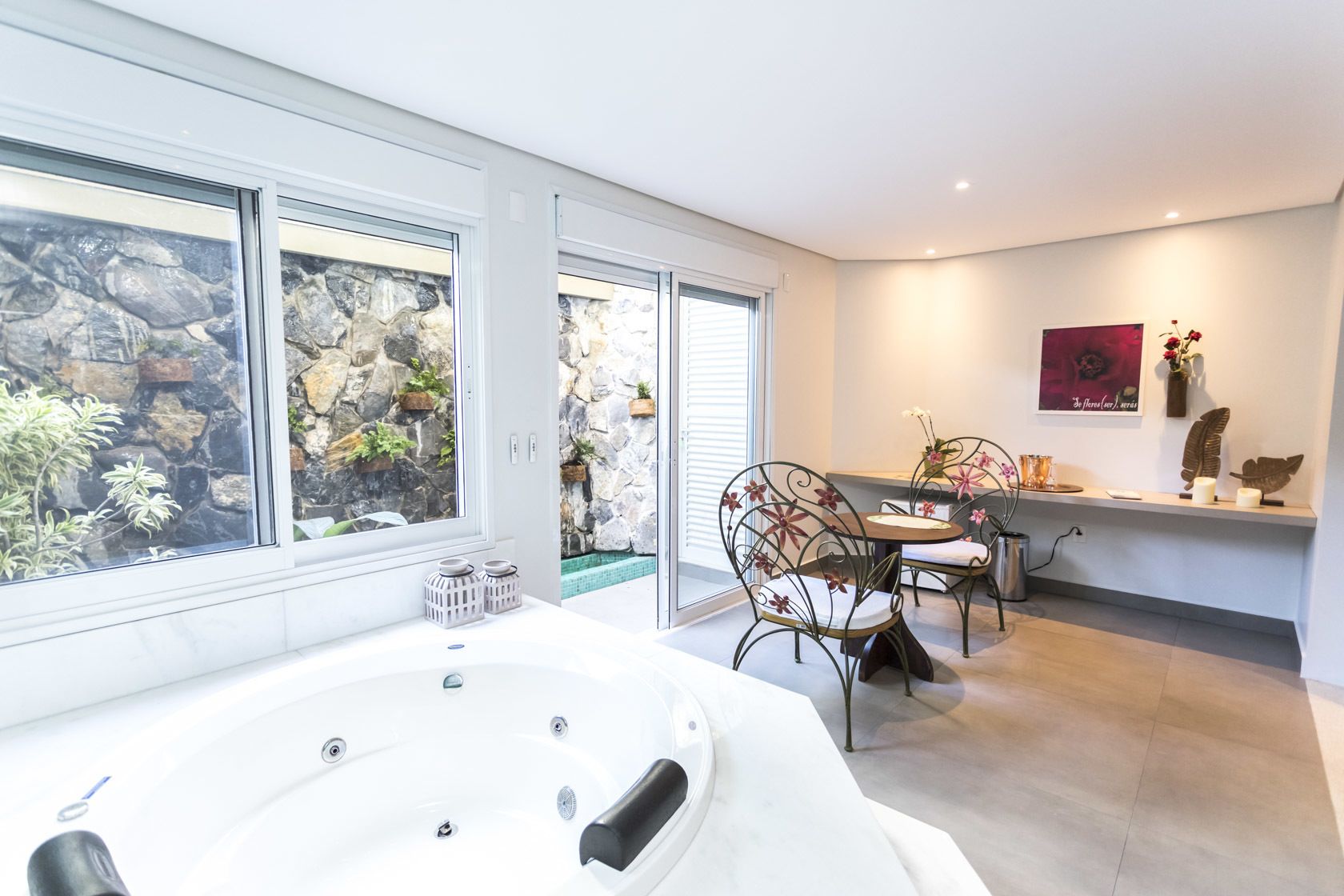 A modern bathroom with a large bathtub, a shower area, and a window with a view of a rocky garden.