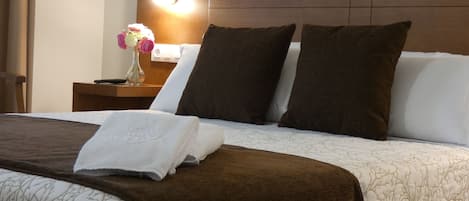 Una cama bien hecha con una manta marrón, almohadas blancas y una toalla blanca.