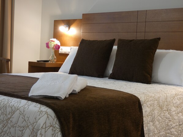 A neatly made bed with a brown blanket, white pillows, and a white towel. - Hotel Arzúa (Arzua)