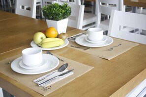 A dining table set with white plates, bowls, and cutlery, accompanied by fruits and a potted plant. - Hotel Arzúa (Arzua)