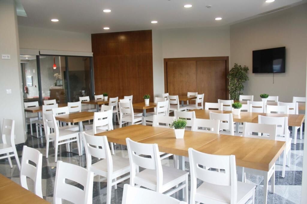 A spacious dining area with multiple tables and chairs, a wooden accent wall, and a television mounted on the wall.