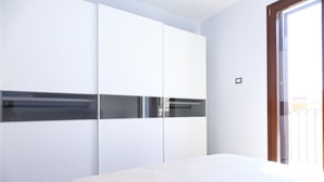 A bedroom with a bed, white wardrobe, and a sliding glass door to the balcony. - Terrazza della Rocca (Cefalù)
