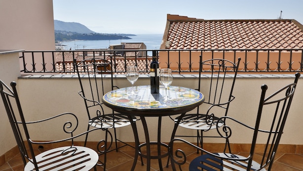 A round table with four chairs and two wine glasses on a balcony overlooking a coastal view. - Terrazza della Rocca (Cefalù)