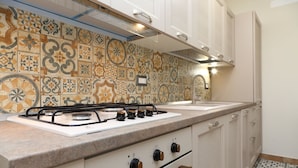 A kitchen with a gas stove, white cabinets, and a patterned backsplash. - Terrazza della Rocca (Cefalù)