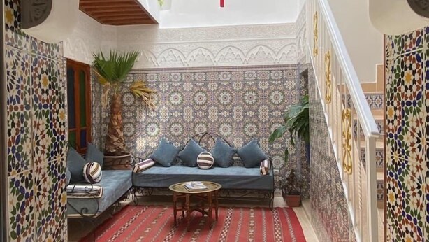 An interior courtyard with a patterned wall, a blue sofa, a red rug, and a hanging lantern. - Dar Dikrayat (Marrakech)
