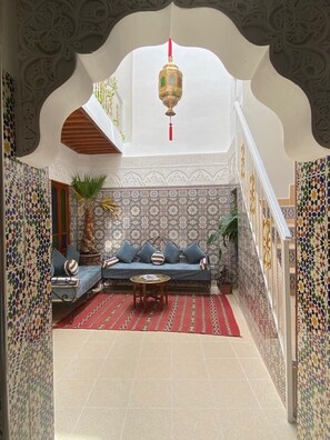 Een Marokkaans interieur met een behang, een bank met kussens, een rood vloerkleed en een hanglamp.