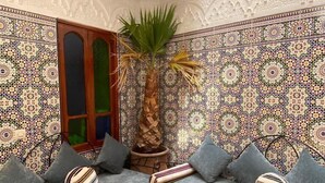 A cozy Moroccan interior with a patterned tile wall, a palm tree, and a sofa with striped cushions. - Dar Dikrayat (Marrakech)