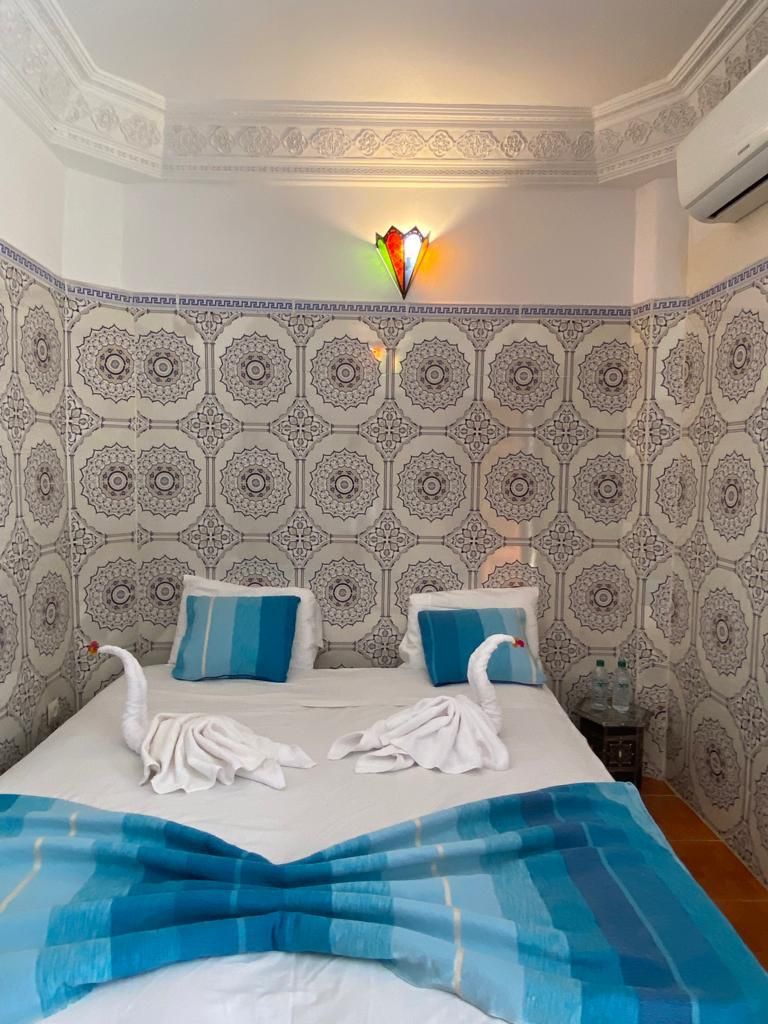 A hotel room with a patterned wallpaper, a bed with blue and white bedding, and a decorative wall light.