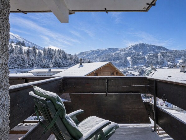 A balcony with a view of snow-covered mountains and a wooden cabin in the distance.
