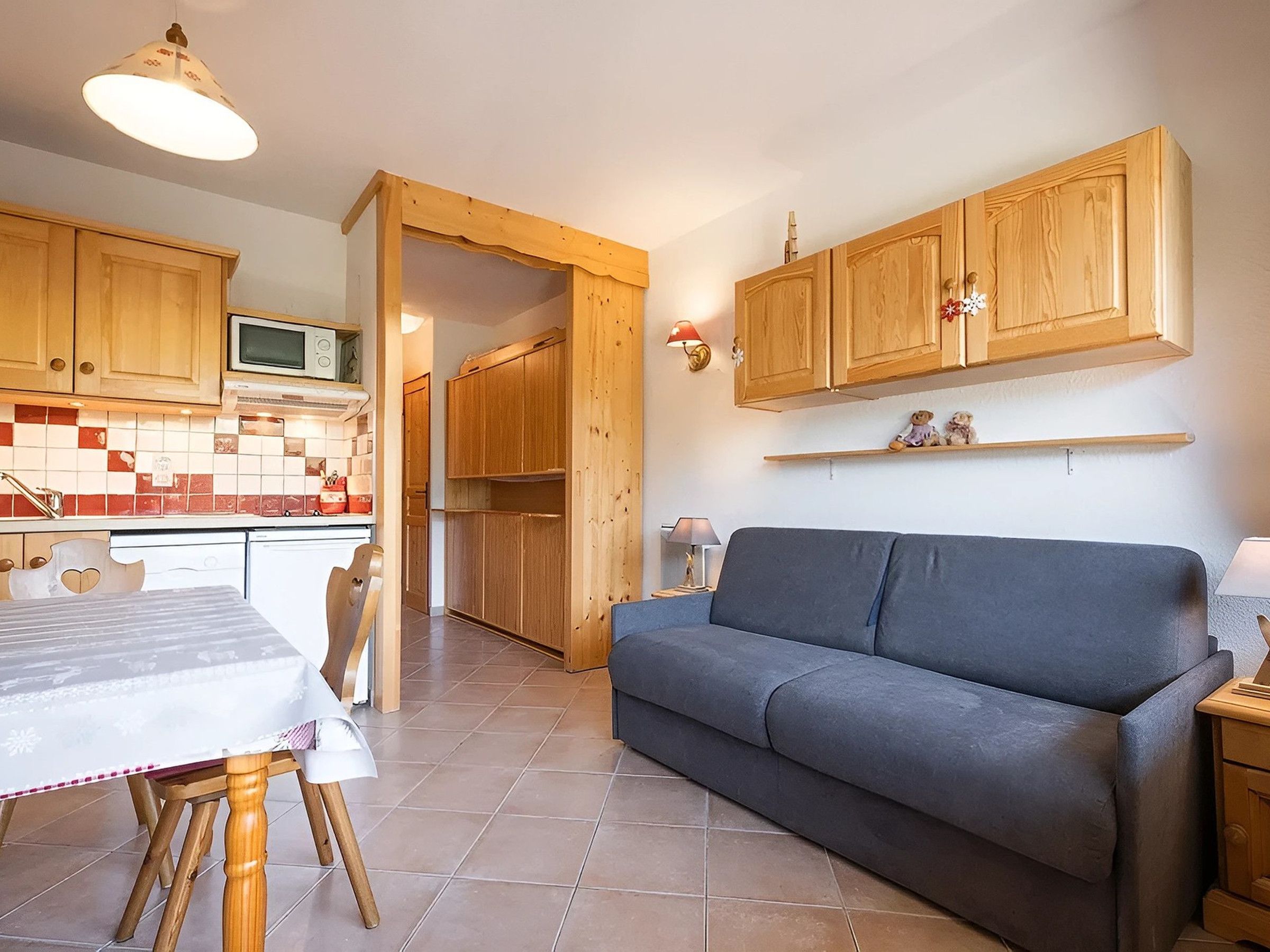 Una cocina compacta con armarios de madera, una mesa de comedor con sillas y un sofá gris en una sala de estar.