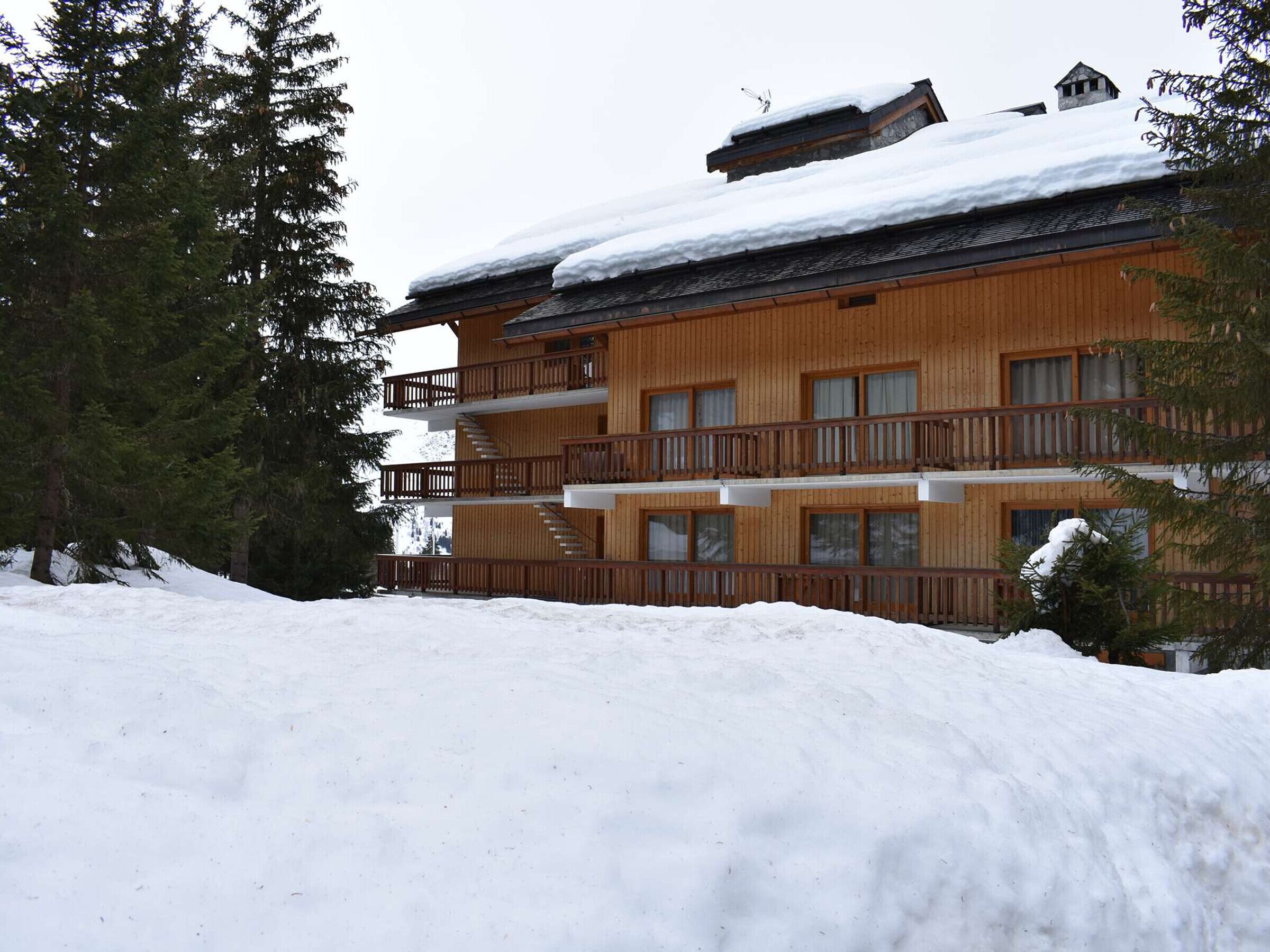 A multi-story wooden building with balconies, surrounded by snow and trees.