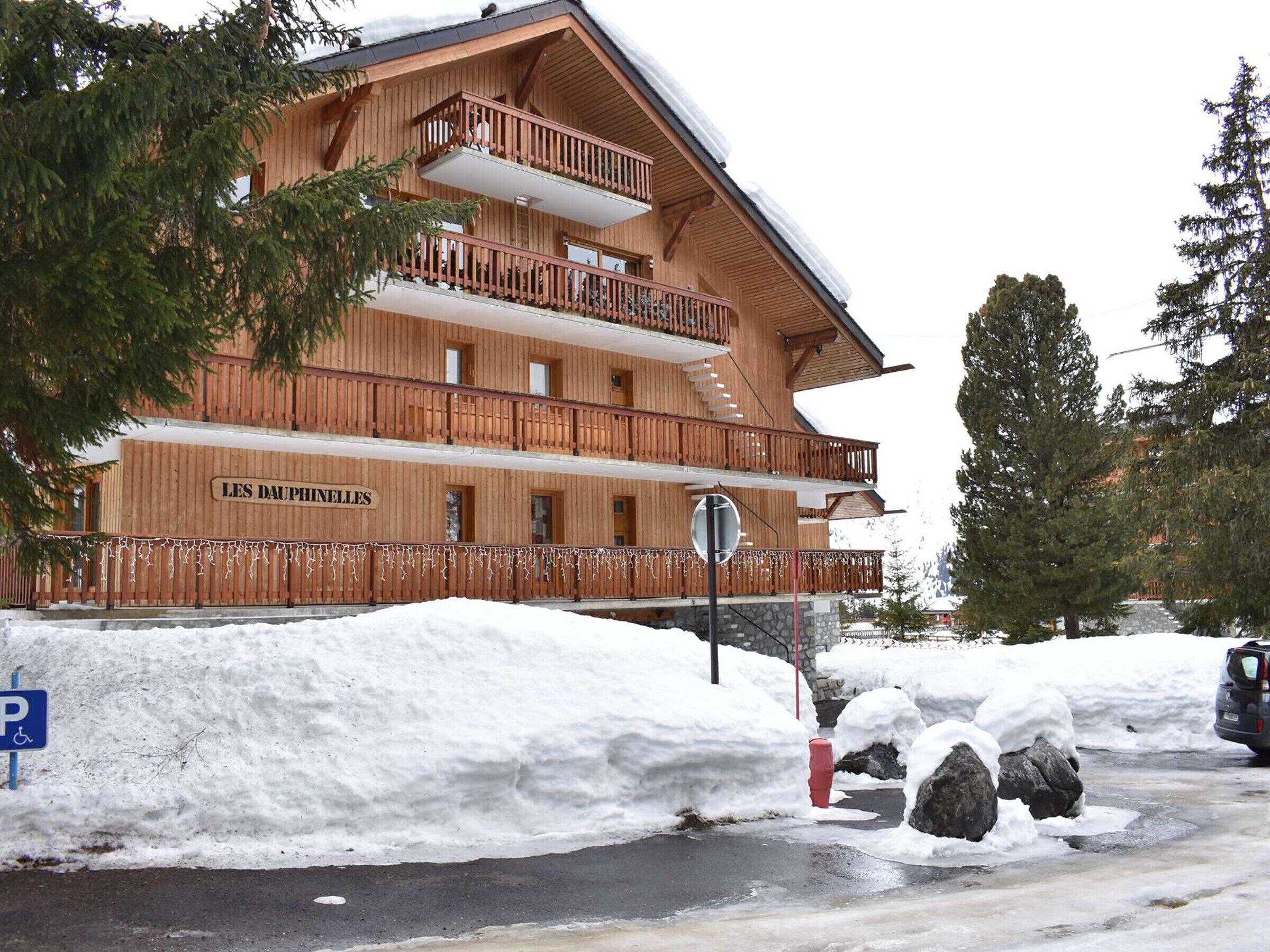 Ein mehrstöckiges Holzgebäude mit Balkonen, einem Schild mit der Aufschrift 'LES DAUPHINELLES' und einem mit Schnee bedeckten Boden.