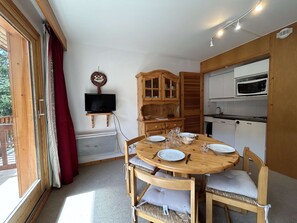 A dining area with a wooden table set for four, a television on a stand, and a kitchen with a microwave.
