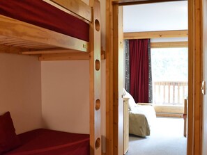 Quarto com beliches, teto de madeira e porta que dá para uma varanda com guarda-corpo de madeira.