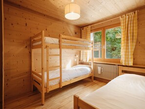 Une chambre avec un lit superposé, une fenêtre, des murs en bois et un radiateur.