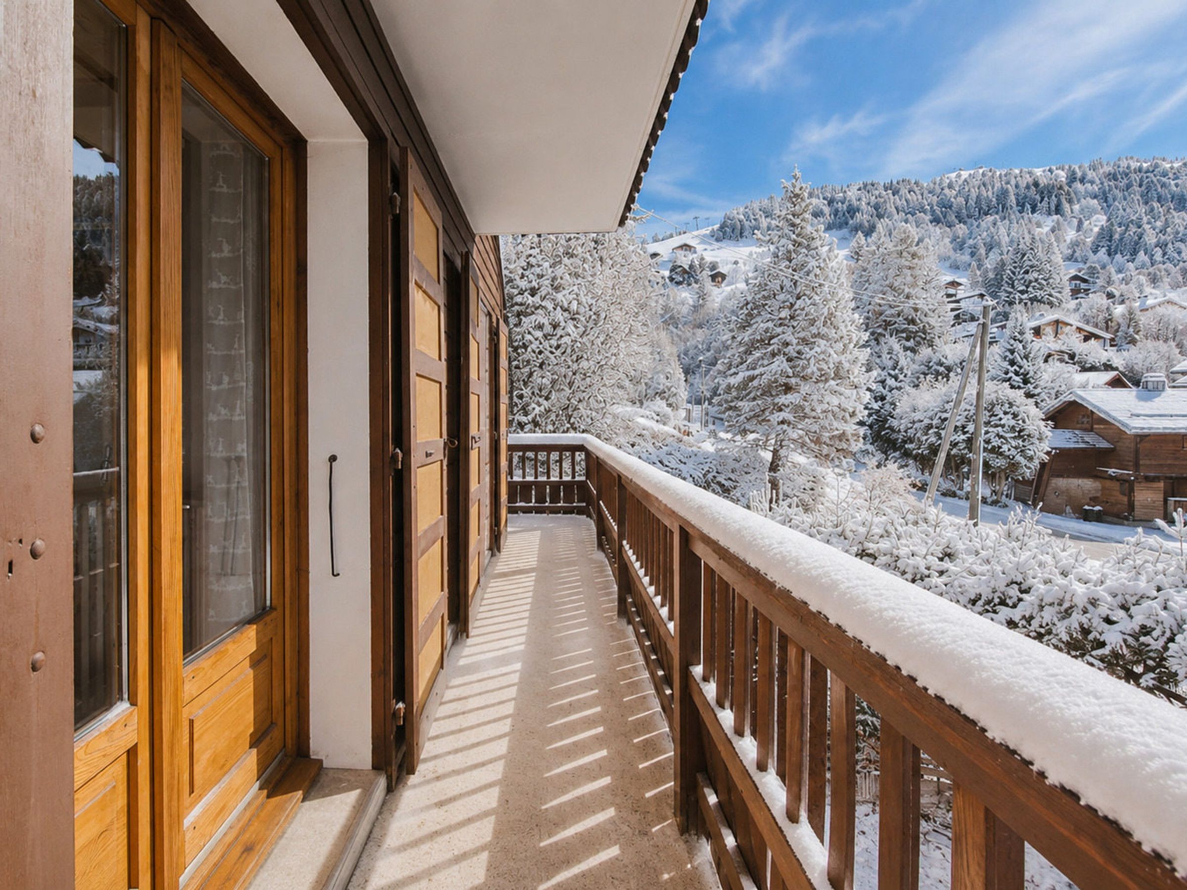 A wooden balcony with a snow-covered railing overlooking a mountainous landscape.