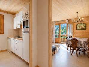 A kitchen with white cabinets, a stove, and a dishwasher. There is a dining area with a table and chairs, and a view of the outdoors through a large window.