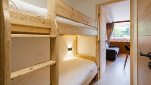 Ein Schlafzimmer mit Etagenbetten, Holzvertäfelung, einem Fenster mit Aussicht und einer Tür zu einem anderen Raum.