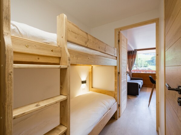A bunk bed room with a wooden interior, a window with a view, and a door leading to another room.