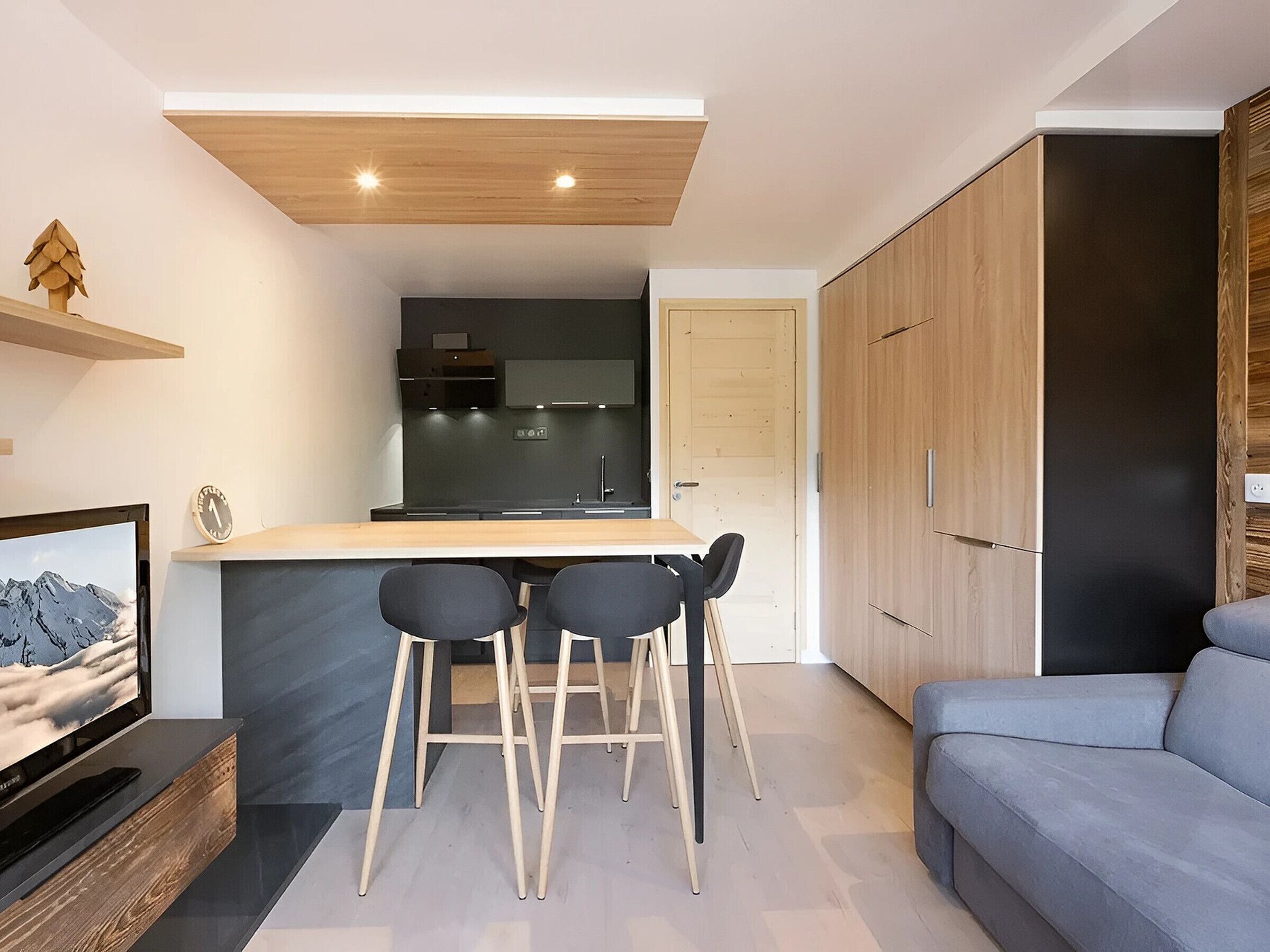 A modern kitchen with a wooden ceiling, a bar area with stools, and a grey sofa.