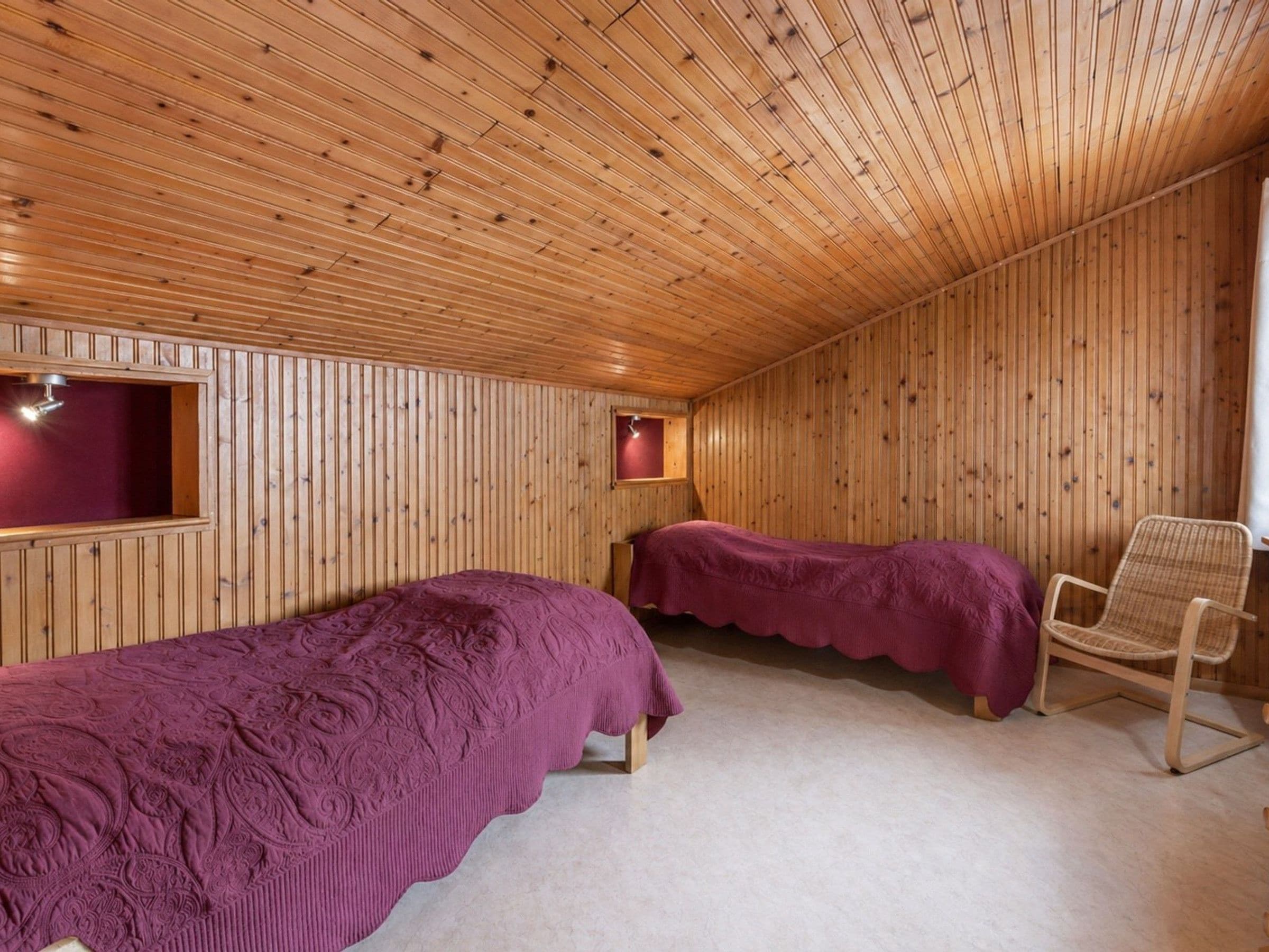 A wooden-paneled room with two beds, a chair, and a small window.