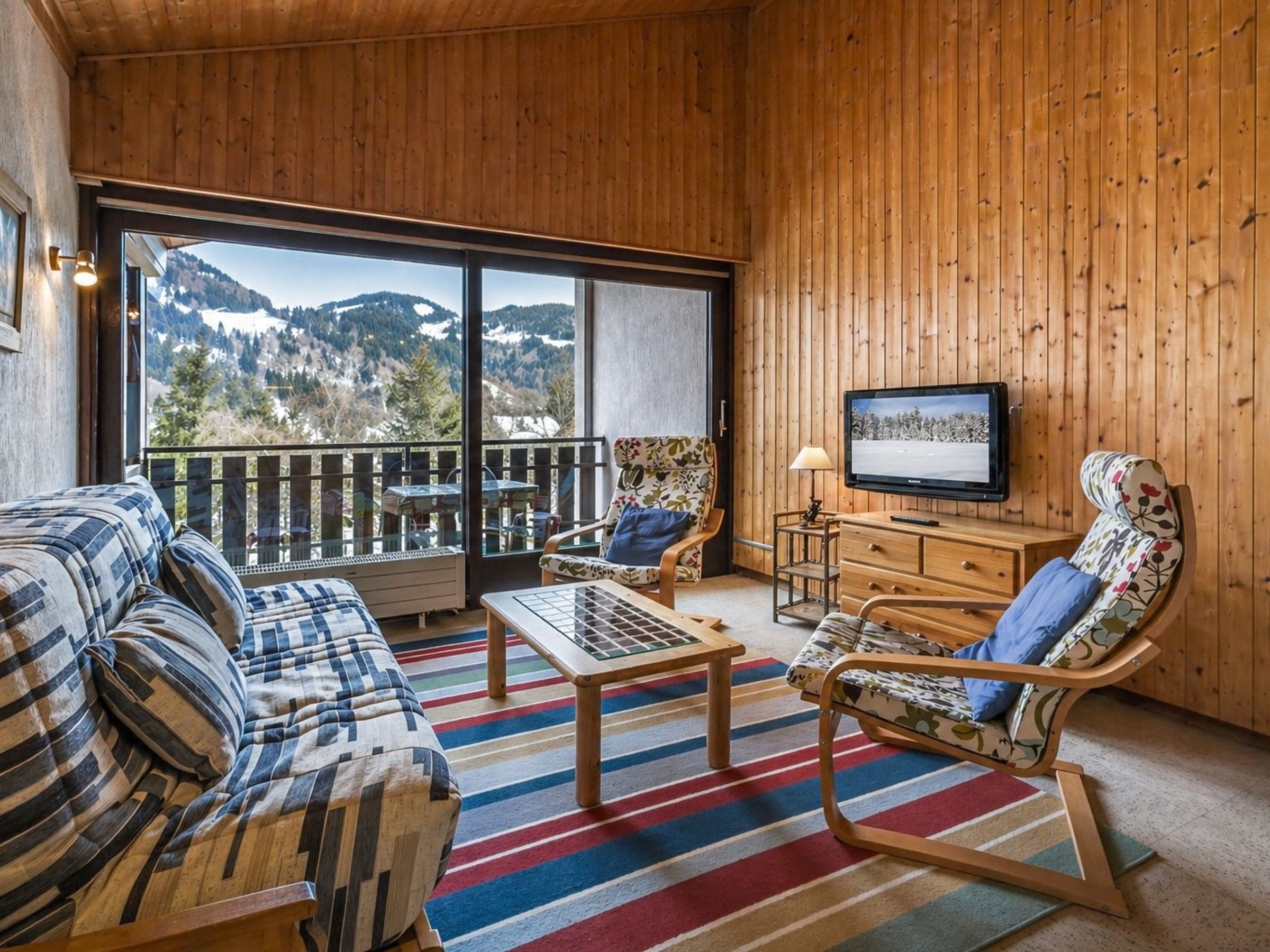 Une pièce confortable avec un canapé, un fauteuil, une télévision et une vue sur les montagnes.