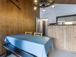 A room with a wooden wall, a dining table with a blue tablecloth, a bench, and a kitchen area with a wooden counter and cabinets. - Spacious 3-bedroom apartment near slopes, pets allowed, parking (La Clusaz)