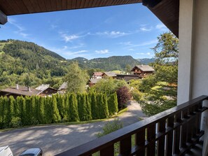 A view from a balcony overlooking a rural landscape with houses, a road, and mountains. - Spacious 3-bedroom apartment near slopes, pets allowed, parking (La Clusaz)