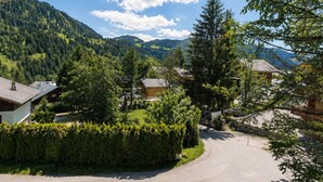 A rural road curving through a village with houses, dense greenery, and mountains in the background. - Spacious 3-bedroom apartment near slopes, pets allowed, parking (La Clusaz)