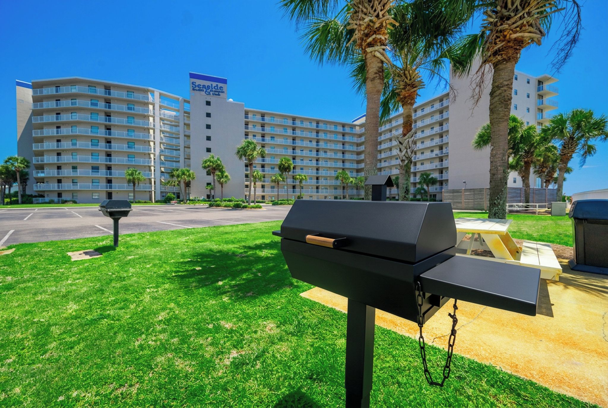 Una parrilla de barbacoa en un área con césped, con un edificio de hotel al fondo.