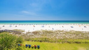 A beach with a wooden walkway, beach chairs, umbrellas, and a flag. - Luxurious Beachfront Corner Unit at Seaside Beach & Racquet 4407 (Orange Beach)