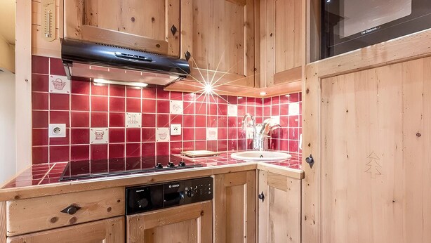 Een keuken met houten kastjes, een rode betegelde achterwand, een fornuis en een vaatwasser.