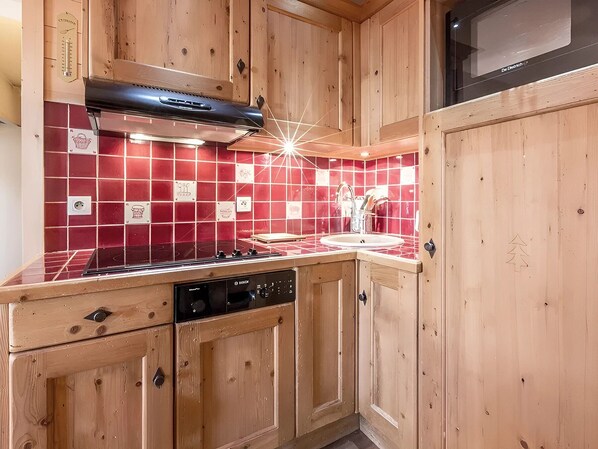 Une cuisine avec des meubles en bois, un plan de travail recouvert de carreaux rouges, une cuisinière et un lave-vaisselle.