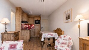 Ein gemütliches Zimmer mit Holzboden, einem Esstisch mit Stühlen, einer Küchenzeile mit Holzausbau und einer Deckenleuchte.
