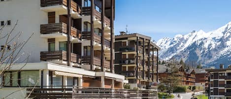 Un hôtel à plusieurs étages doté de balcons, avec une piste de ski en arrière-plan et un ciel dégagé.
