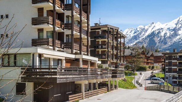 Ein mehrstöckiges Hotel mit Balkonen, im Hintergrund ein Skiabhang und ein klarer Himmel.